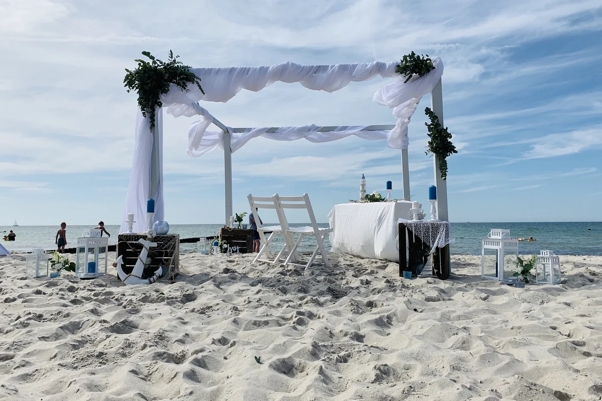 Dekorierter Traupavillon mit weißen Tuechern und Gruenschmuck am Strand von Warnemünde, dahinter die Ostsee
